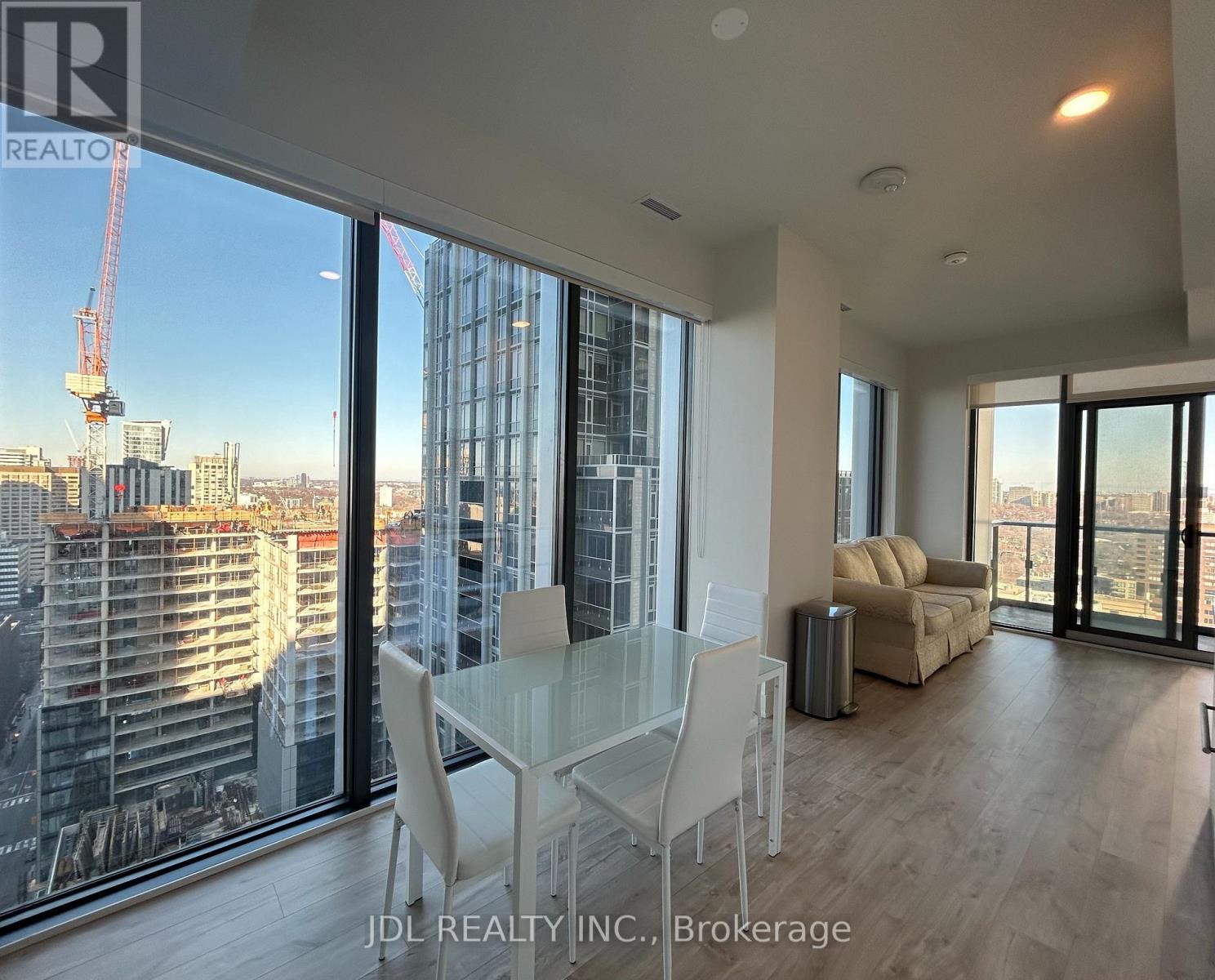 A modern living room with a glass table and chairs, overlooking a cityscape.