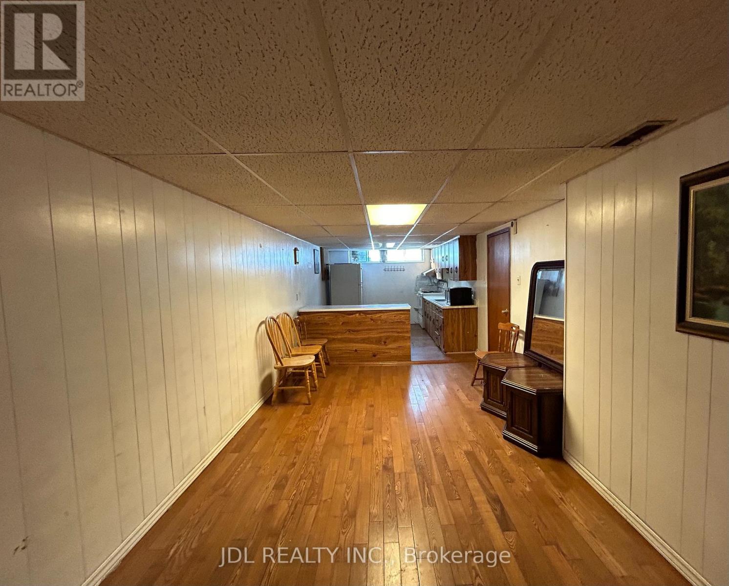 A room with wooden floors and white walls, furnished with a couch, chairs, and a television.