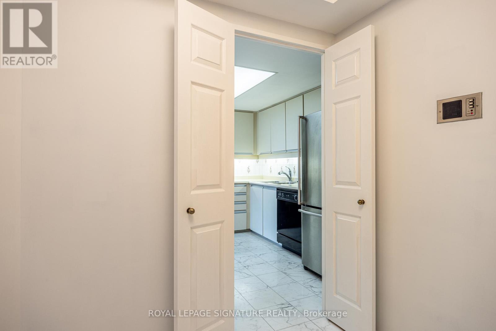 A white door opens to a kitchen with white cabinets and a black fridge.