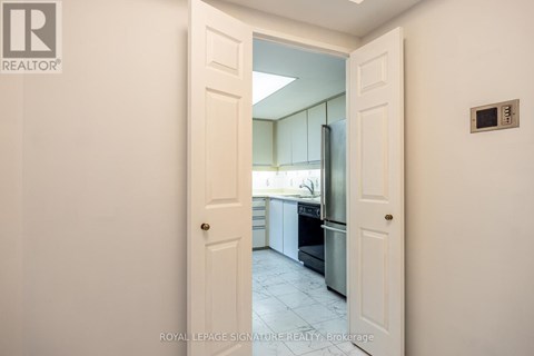 A white door opens to a kitchen with white cabinets and a black fridge.