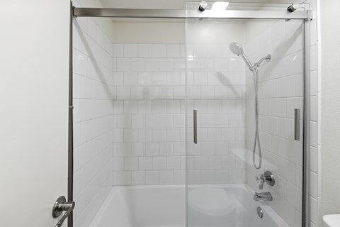 A white tiled shower with a glass door and a shower head.