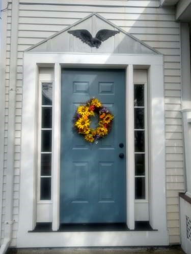 A blue door with a wreath and a black bird on top.