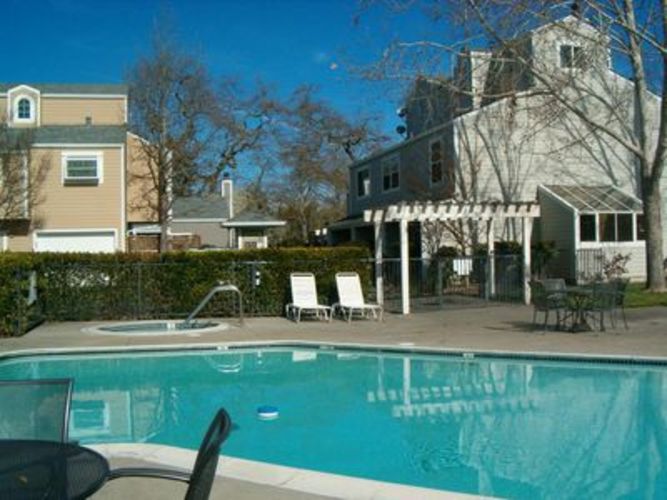 A pool with a chair and table in front of a house.
