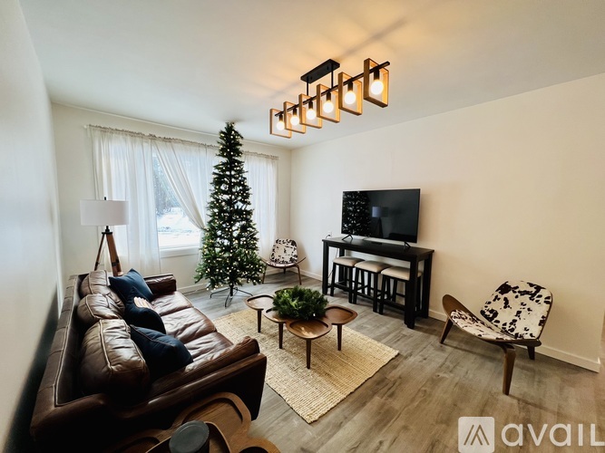 A living room with a brown leather couch, a small table, a chair, a television, and a Christmas tree.