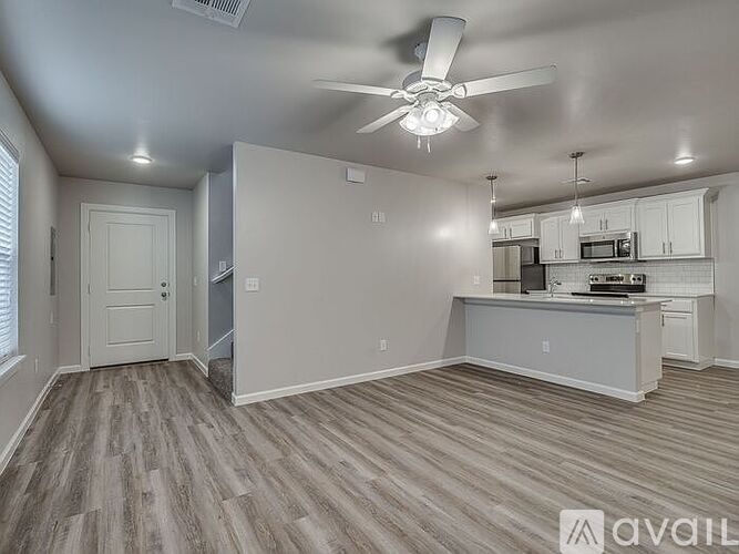 A room with a ceiling fan and a kitchenette in the background.