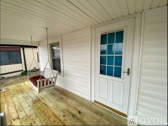 A white house with a wooden deck and a red cushion on it.