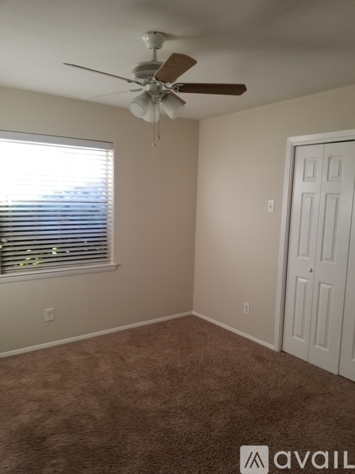 A room with a carpeted floor, a ceiling fan, and a window with blinds.