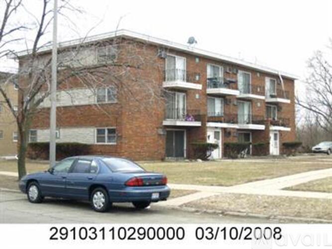 A blue car is parked in front of a brick apartment building.