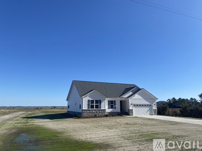 A white house with a grey roof stands alone in a field.
