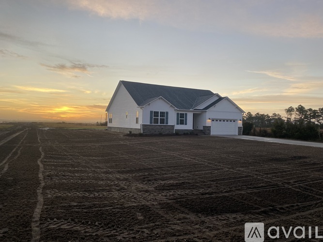 A white house is situated in a field with a sunset in the background.