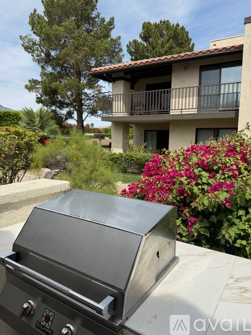 A BBQ grill is in the foreground in front of a house with a balcony.