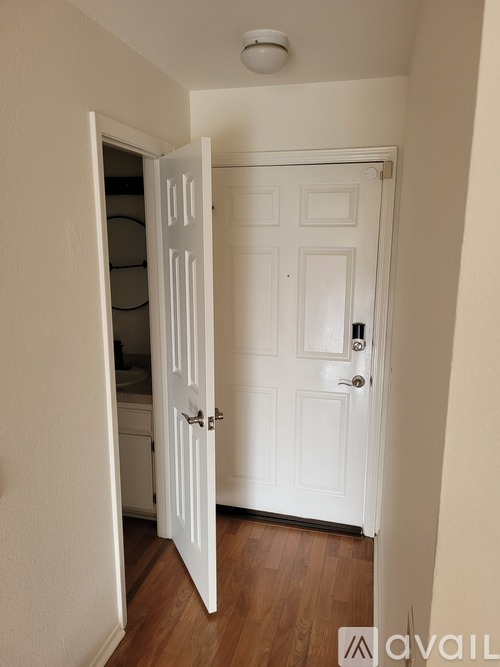 A white door with a black handle is open to a hallway.