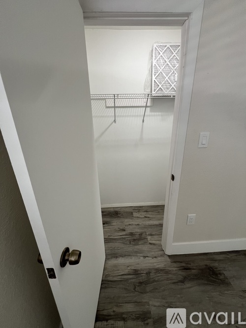 A white door with a black handle is open to a room with a white shelf and a wooden floor.