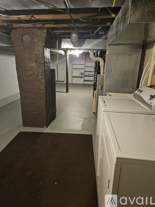 A dirty basement with a brown carpet and white cabinets.