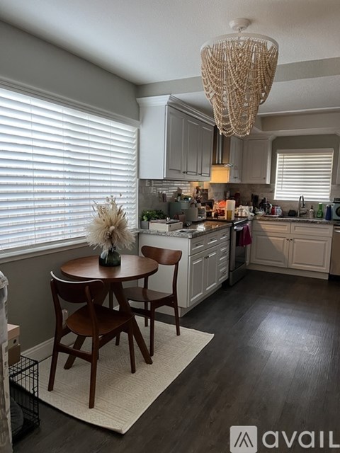 A kitchen with a table and chairs in the foreground and a chandelier hanging from the ceiling.