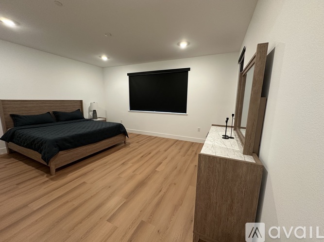 A bedroom with a bed, wooden floor, and a mirror on a wooden stand.