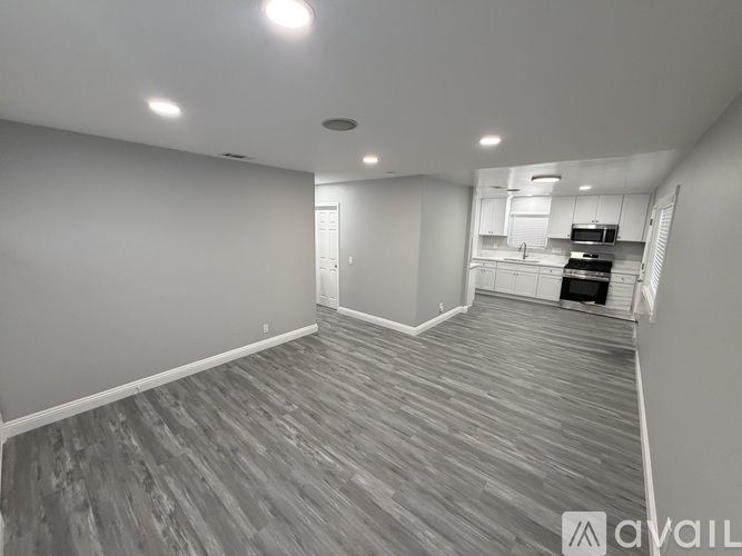 A spacious room with wooden flooring and a kitchen area in the background.