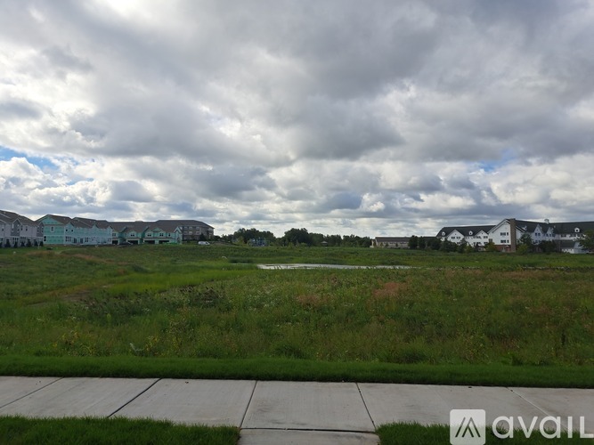 A grassy field with a cloudy sky and houses in the distance.
