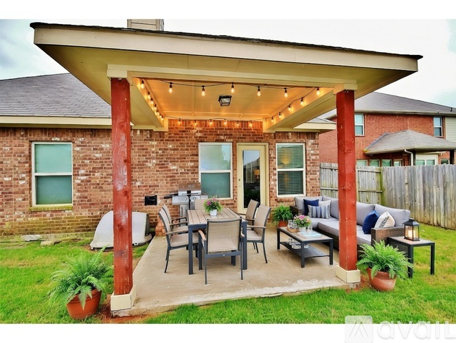 A covered patio with a table and chairs is in front of a brick house.