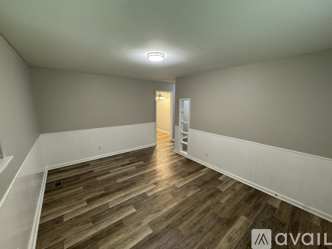A room with wooden flooring and white walls, with a door at the end of the hallway.