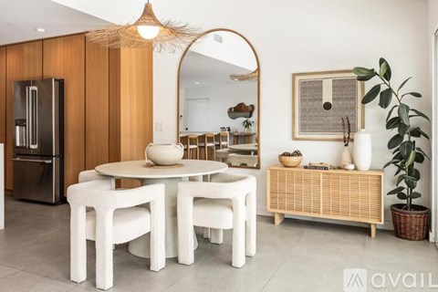 A modern dining room with a white table and chairs, a wooden cabinet, and a mirror on the wall.