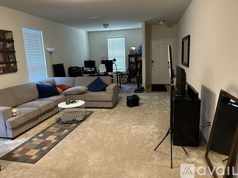 A living room with a couch, a chair, a coffee table, a guitar, a camera, a tripod, a television, and a bookshelf.