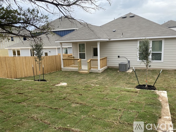 A backyard with a fence, a tree, and a house.