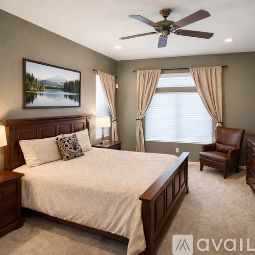 A bedroom with a large bed, a painting on the wall, a ceiling fan, and a chair.