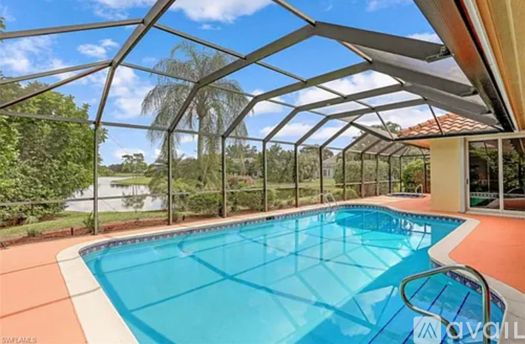 A swimming pool under a glass roof with trees in the background.