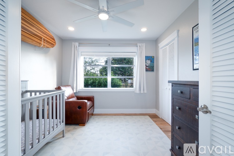 A baby's room with a crib, a brown ottoman, and a window with a view of trees.