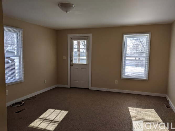 A room with a door, two windows, and a carpeted floor.