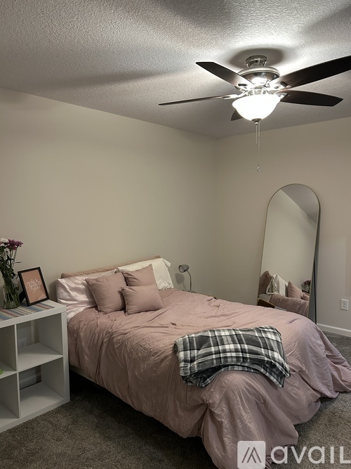 A bedroom with a bed, a ceiling fan, and a mirror.