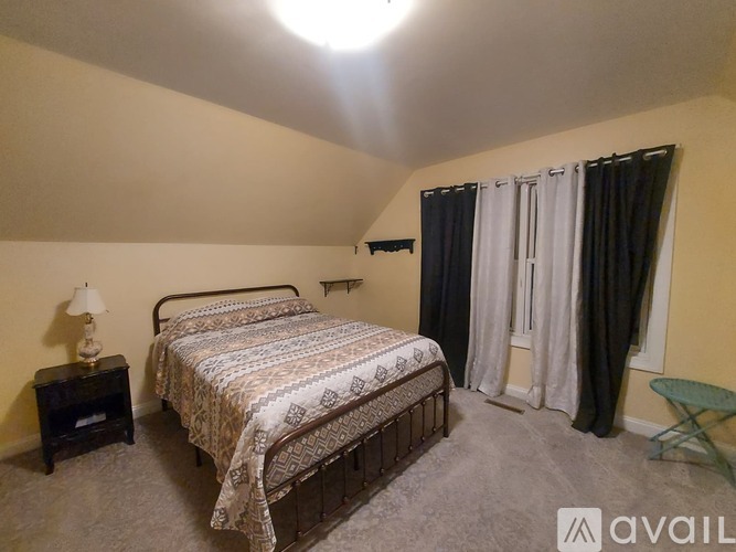 A bedroom with a bed, nightstand, and window with curtains.