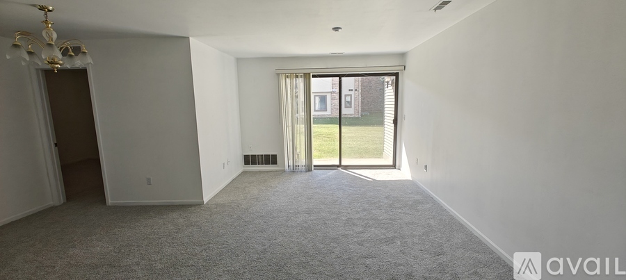 A spacious room with a carpeted floor and a sliding glass door leading to a green outdoor area.