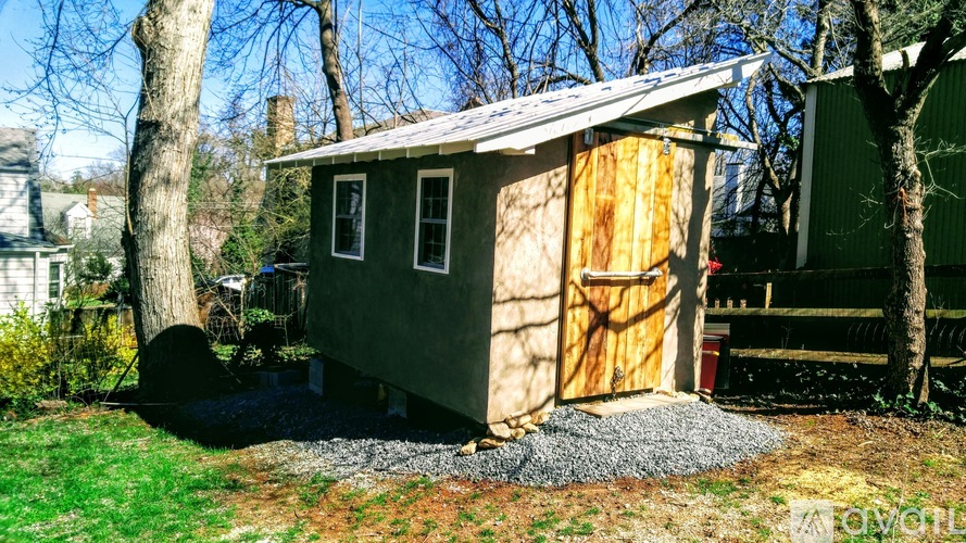 A shed with a grey roof and a yellow door is surrounded by trees.