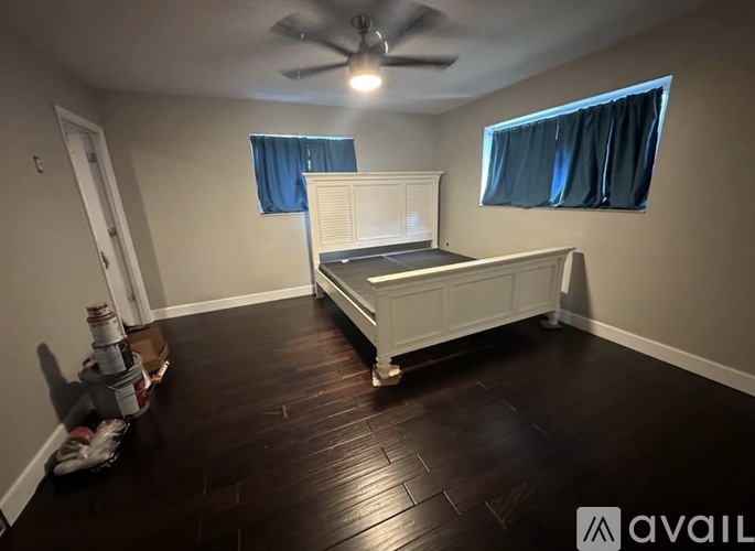 A room with a bed, a ceiling fan, and a window with blue curtains.