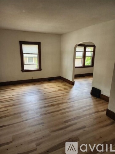A room with wooden flooring and two windows.