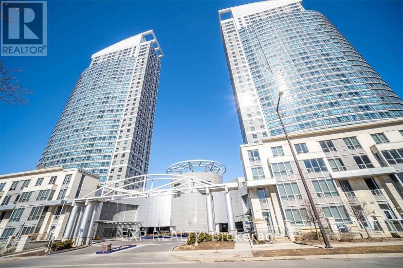 A modern building with a glass facade stands tall in the foreground with another building in the background.