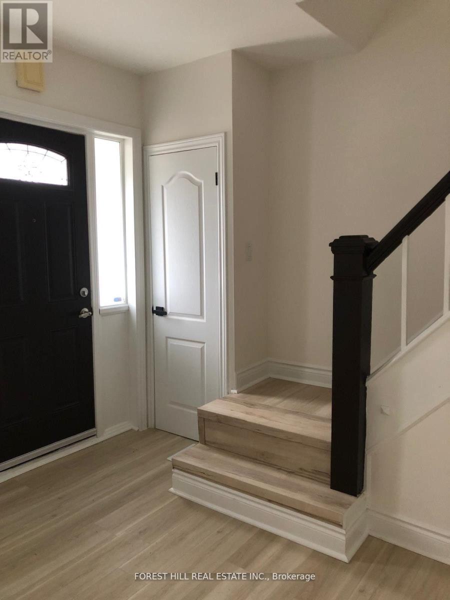 A hallway with a wooden staircase and a black door.