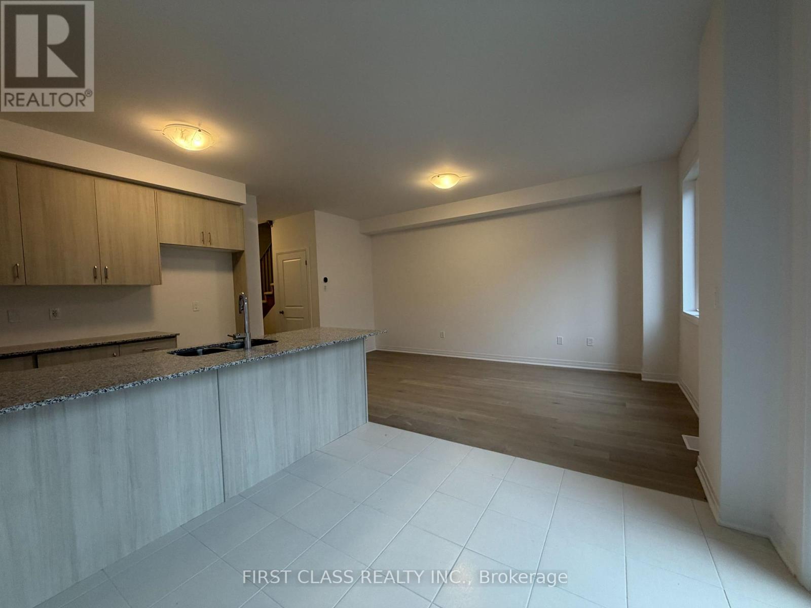 A spacious room with wooden floors and a kitchen area with cabinets and a countertop.