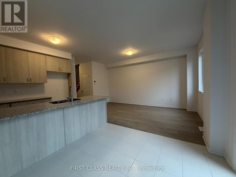 A spacious room with wooden floors and a kitchen area with cabinets and a countertop.