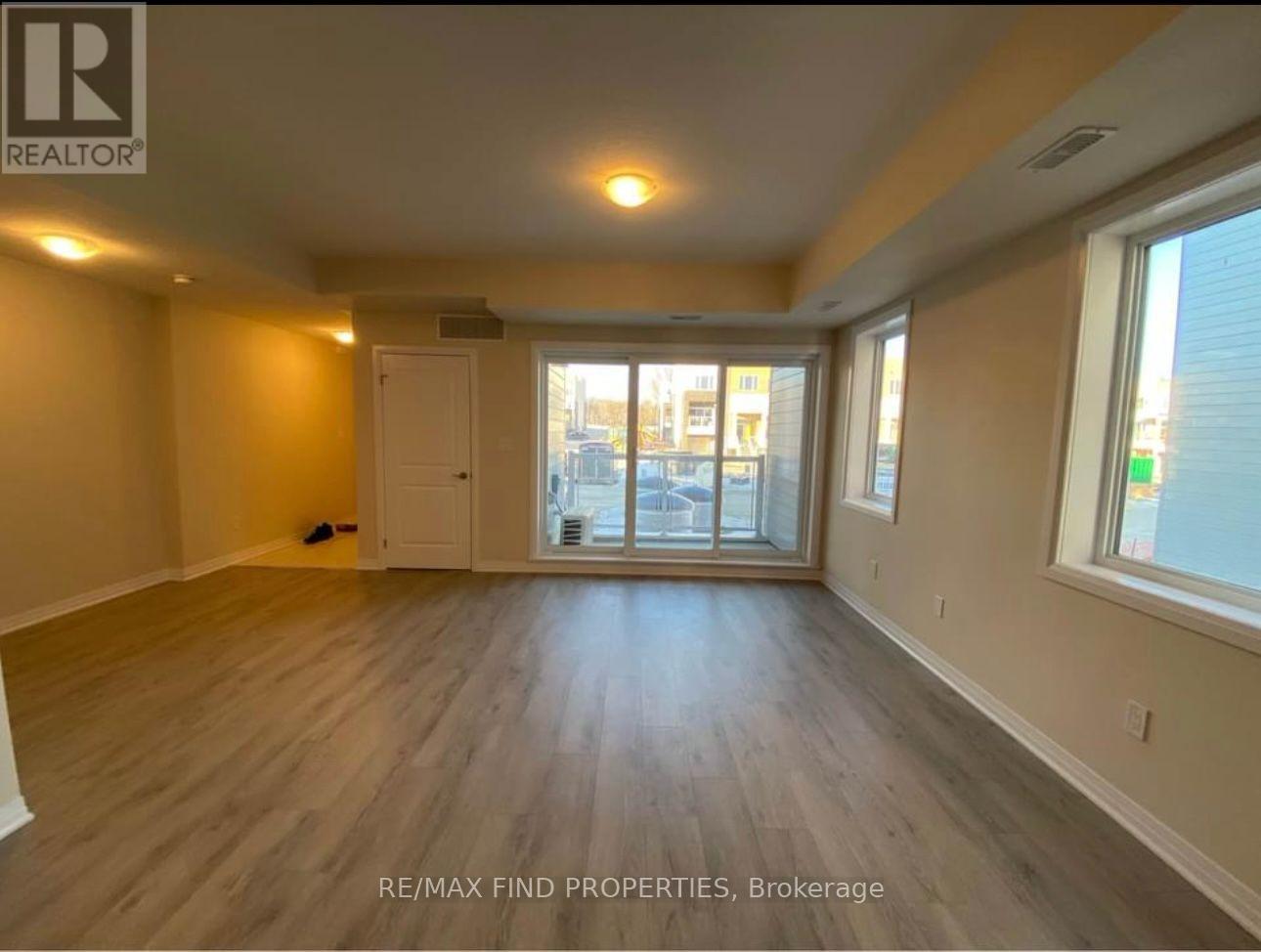 A spacious room with wooden flooring and large windows.