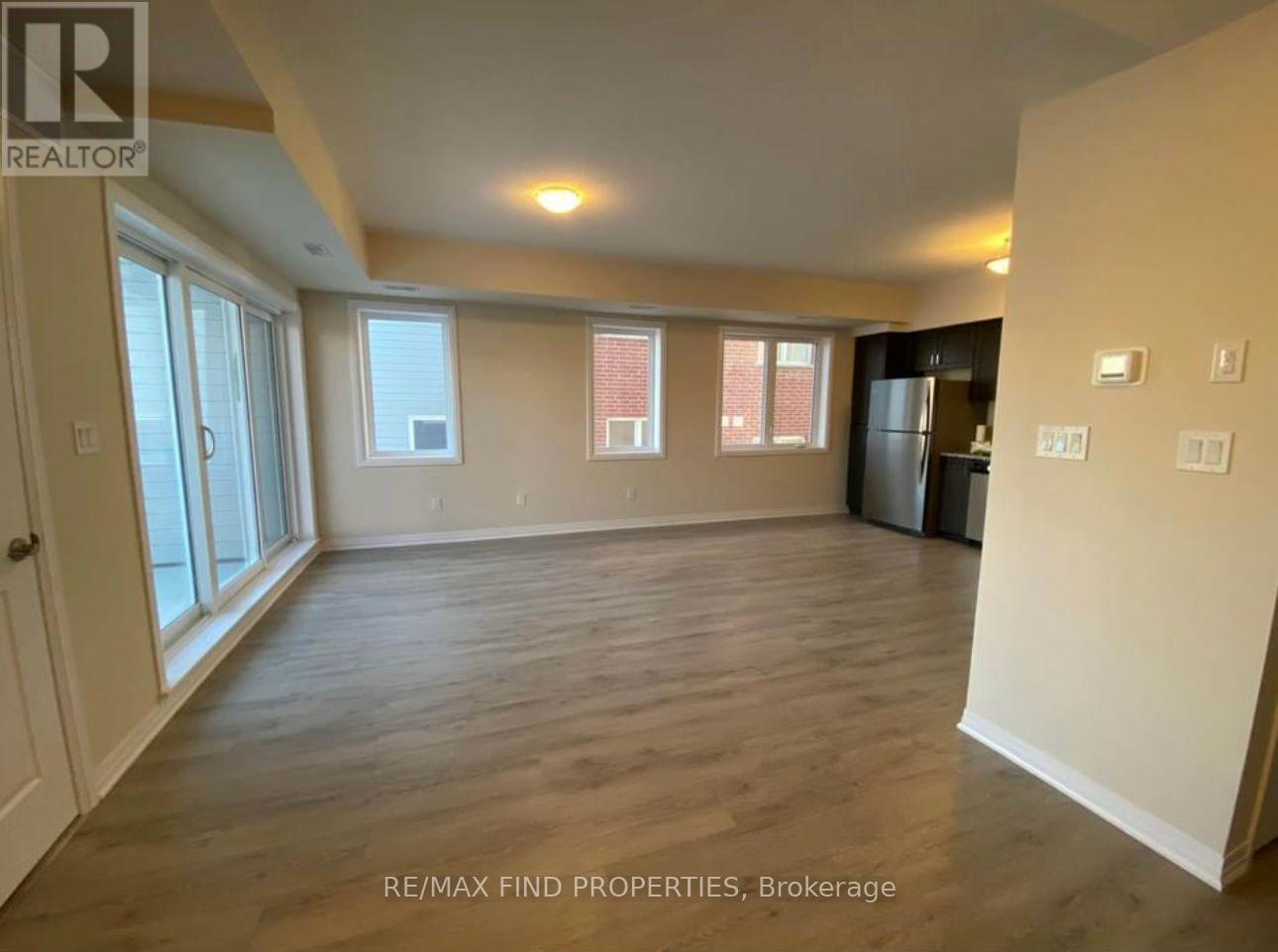 A spacious room with wooden flooring and large windows.