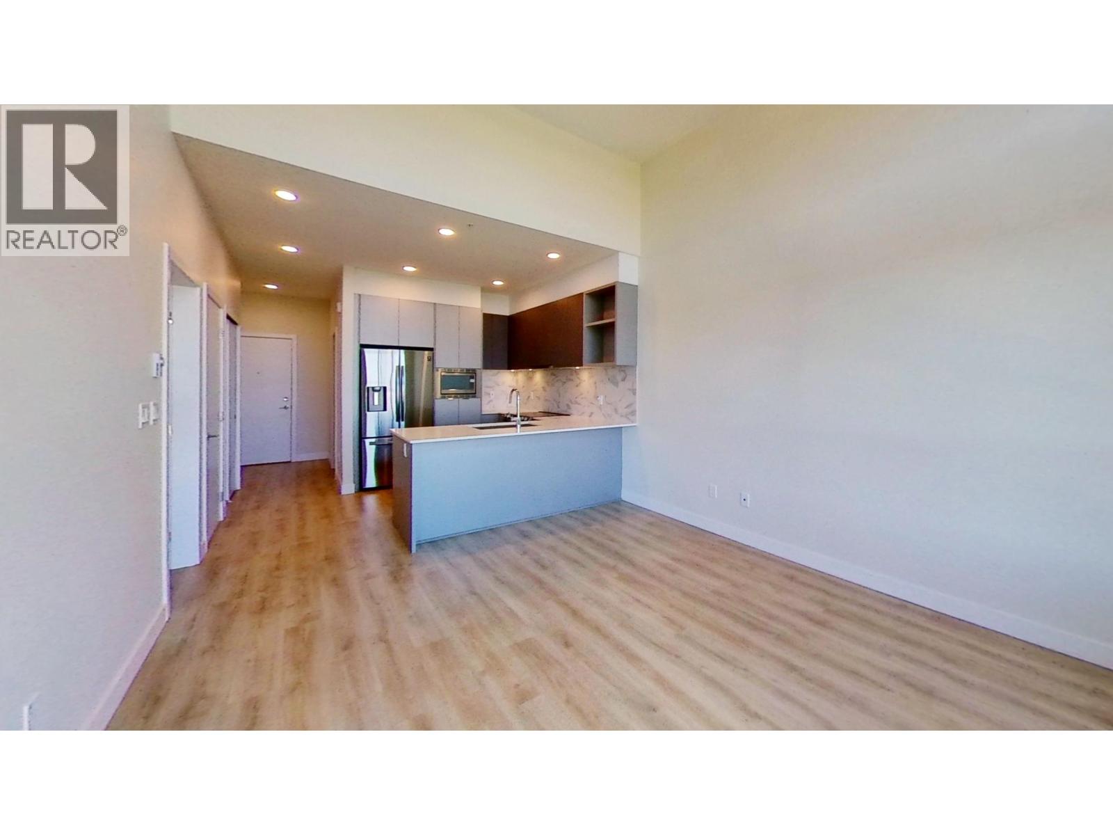 A spacious room with wooden floors and a kitchen area in the background.