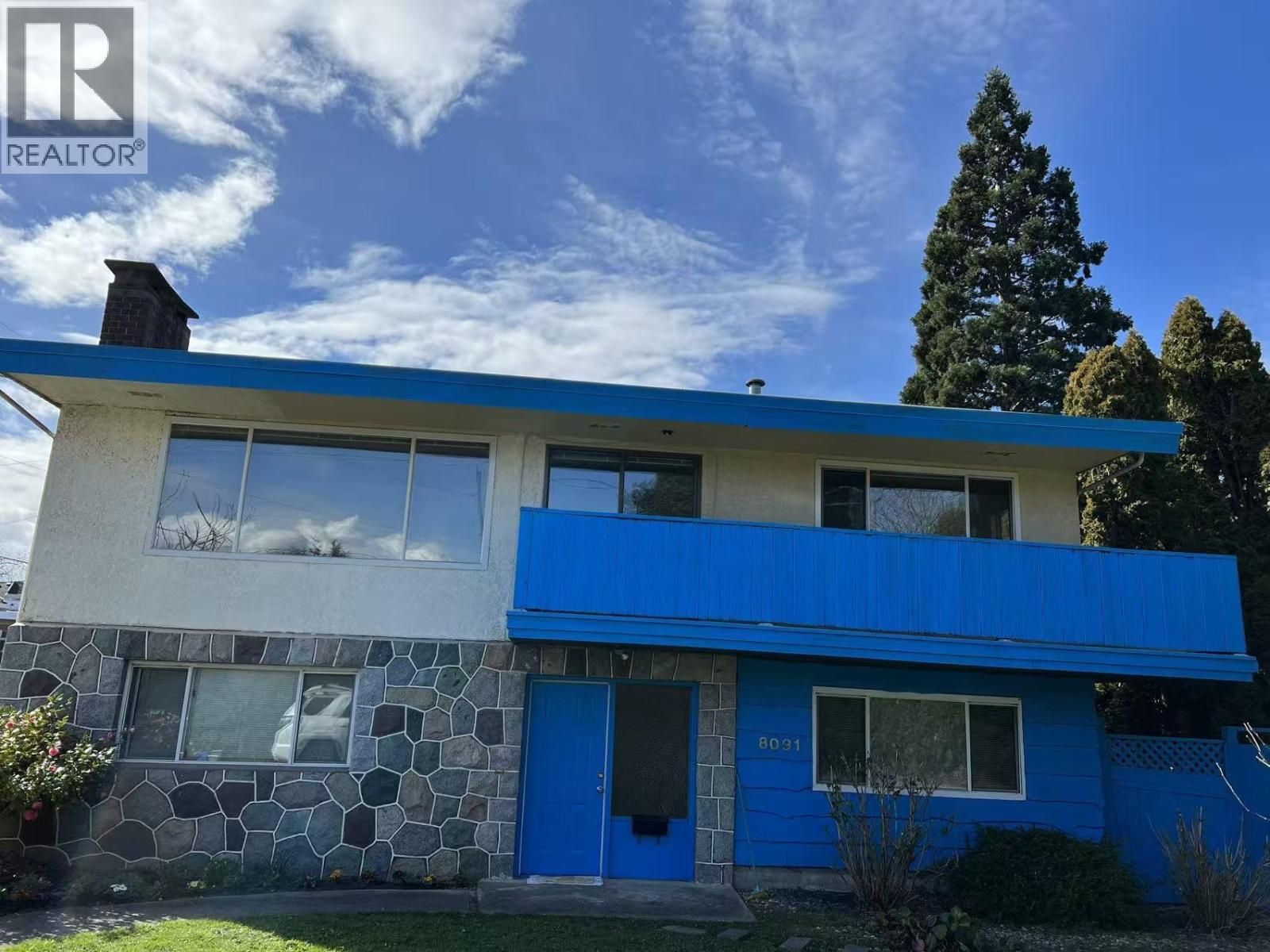 A blue and white house with a stone wall and a tree in the background.