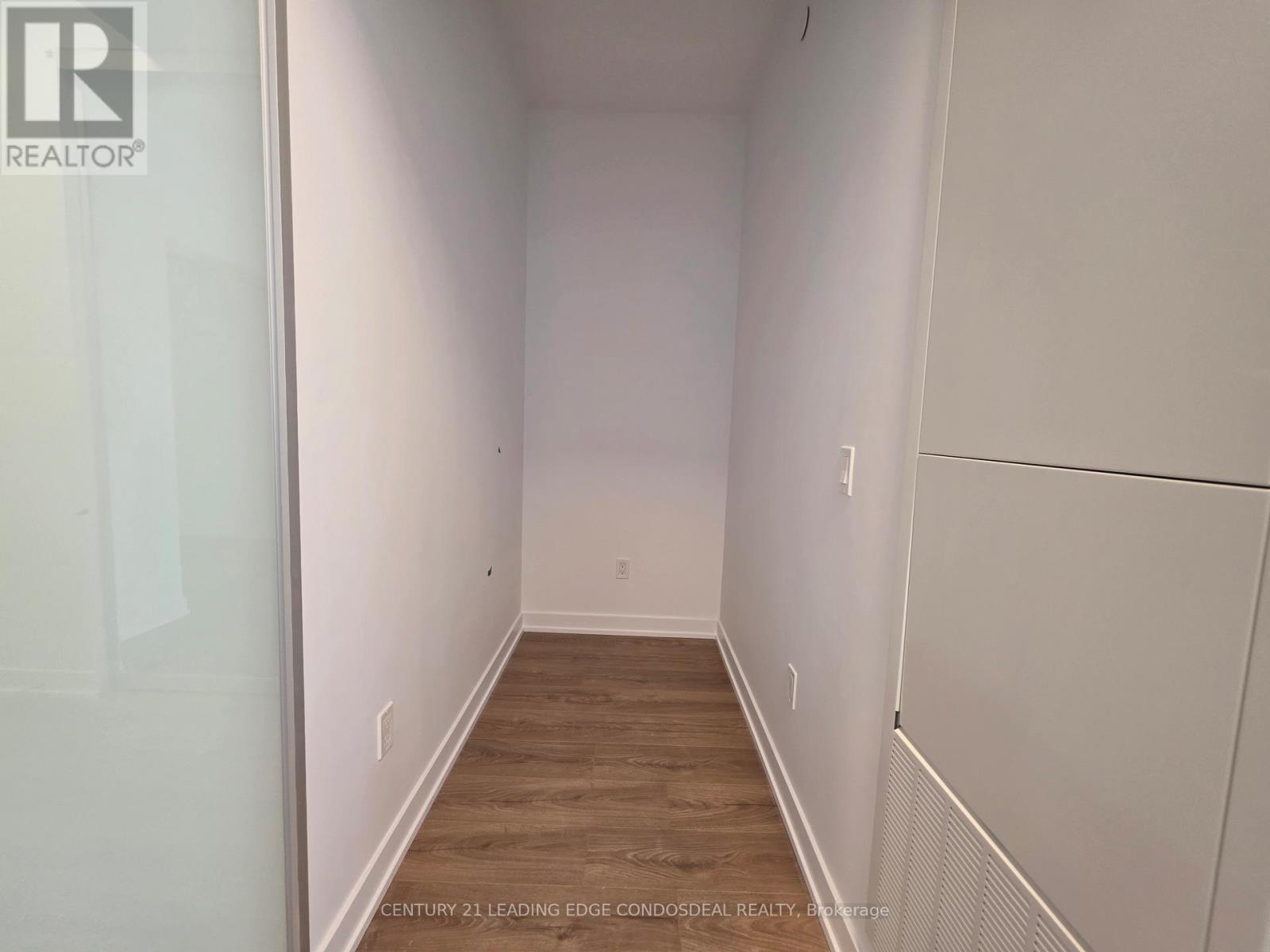 A long, empty hallway with wood flooring and white walls.