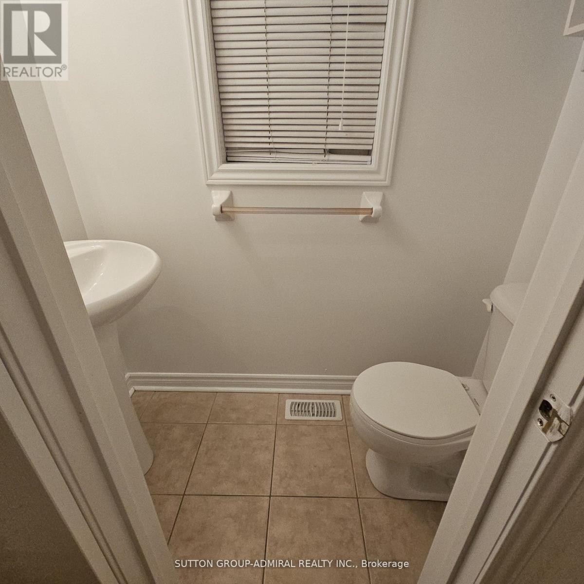A white toilet in a small bathroom with a window above it.
