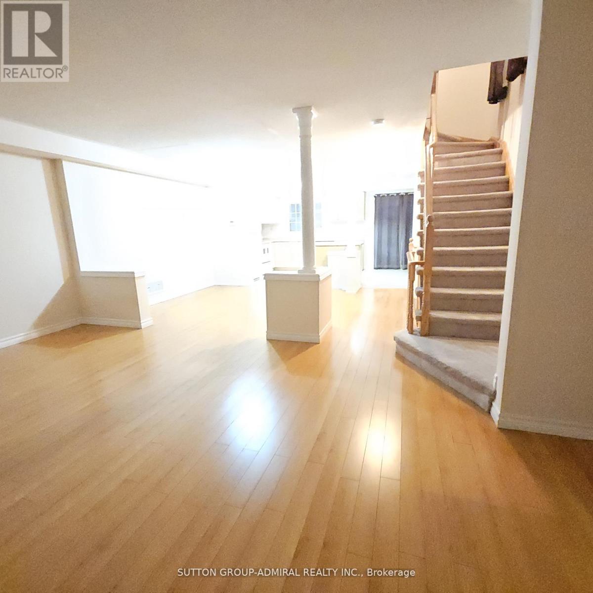 A spacious room with wooden floors and a staircase.