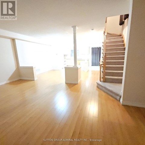 A spacious room with wooden floors and a staircase.