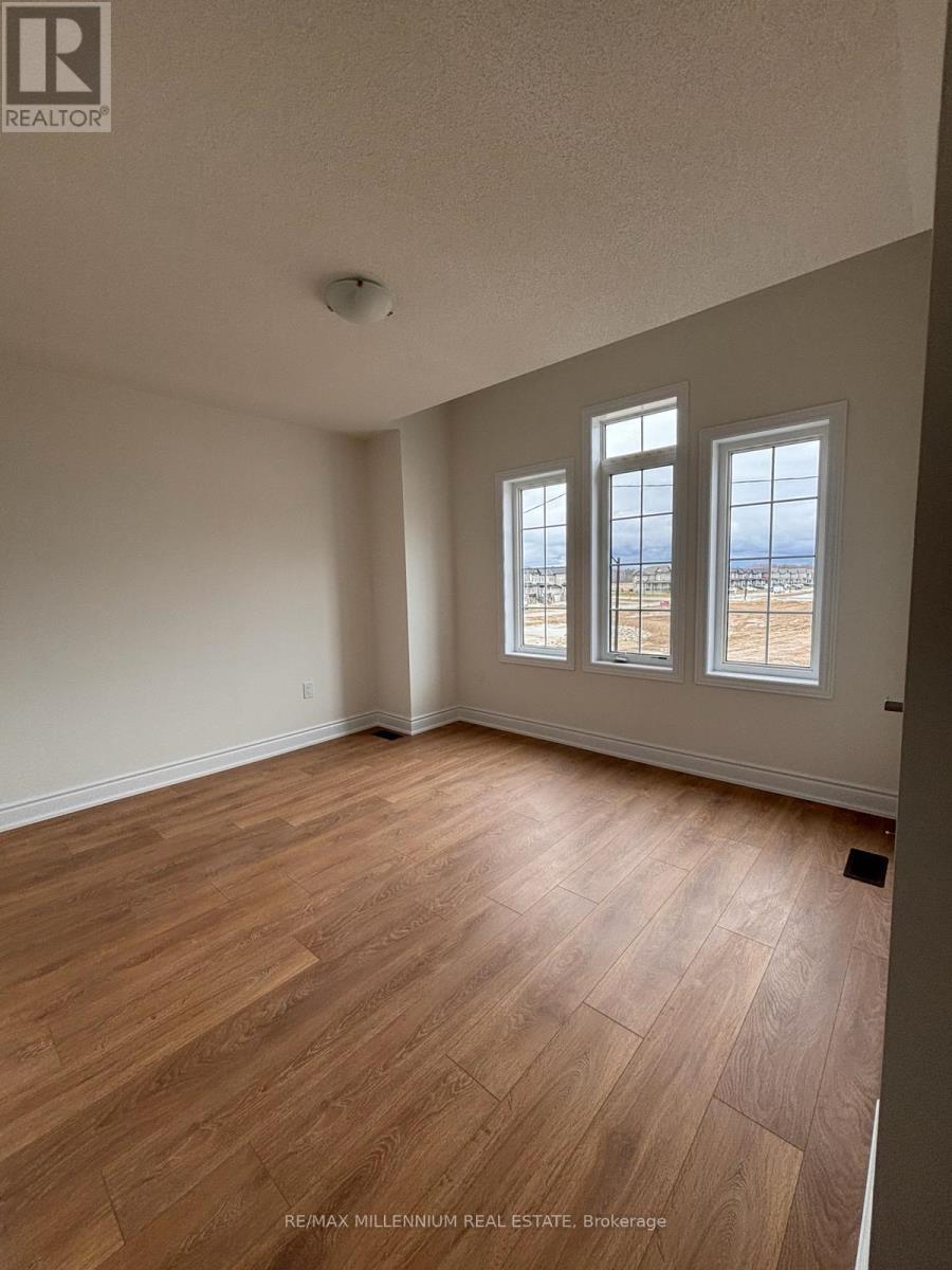 A room with wooden flooring and three windows overlooking a beach.
